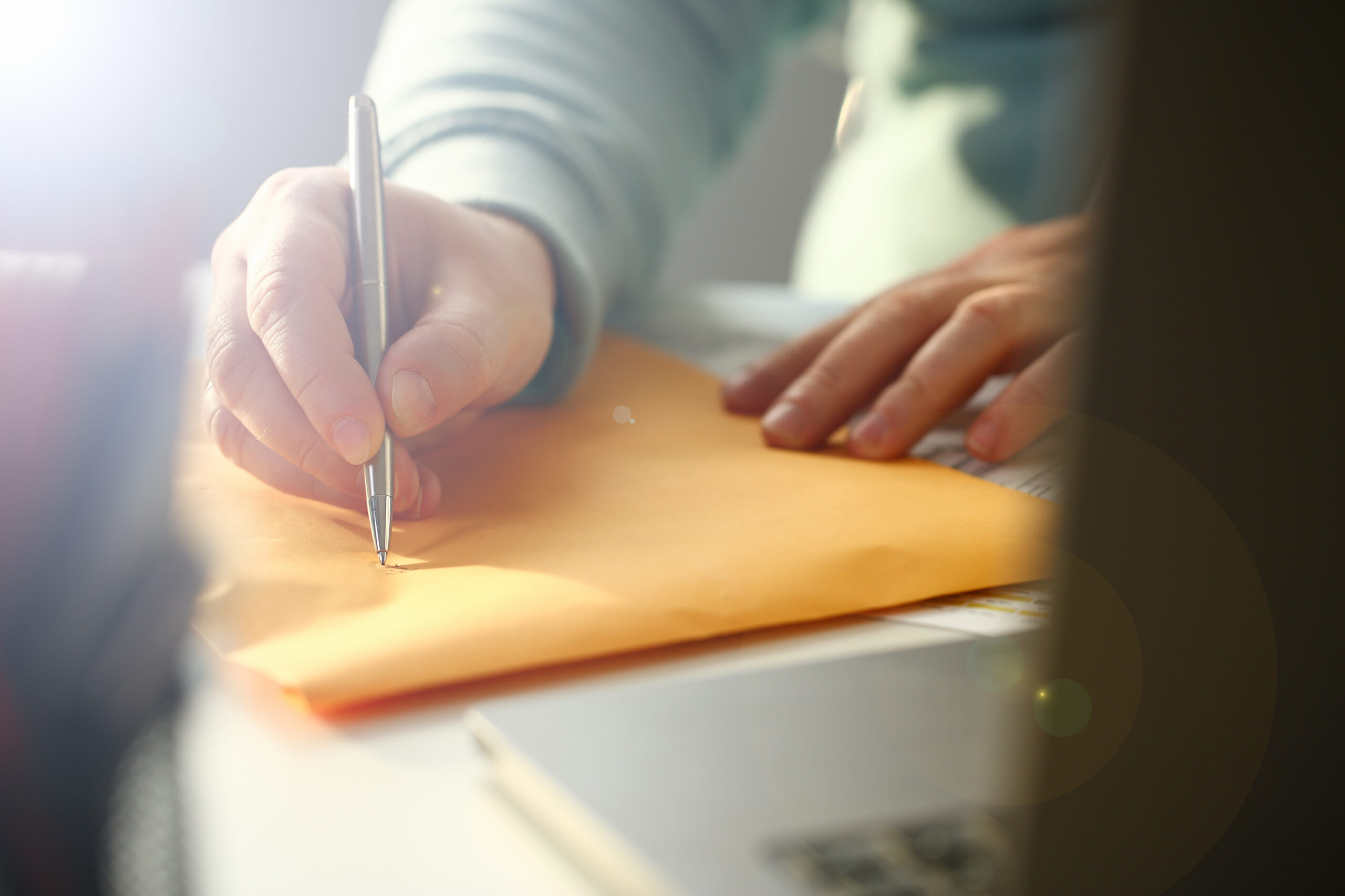 Male hand holding silver pen writing on envelope